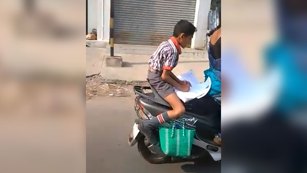 కదిలే స్కూటర్ మీద హోమ్ వర్క్ చేస్తున్న పిల్లాడు కదిలే స్కూటర్ మీద హోమ్ వర్క్ చేస్తున్న పిల్లాడు